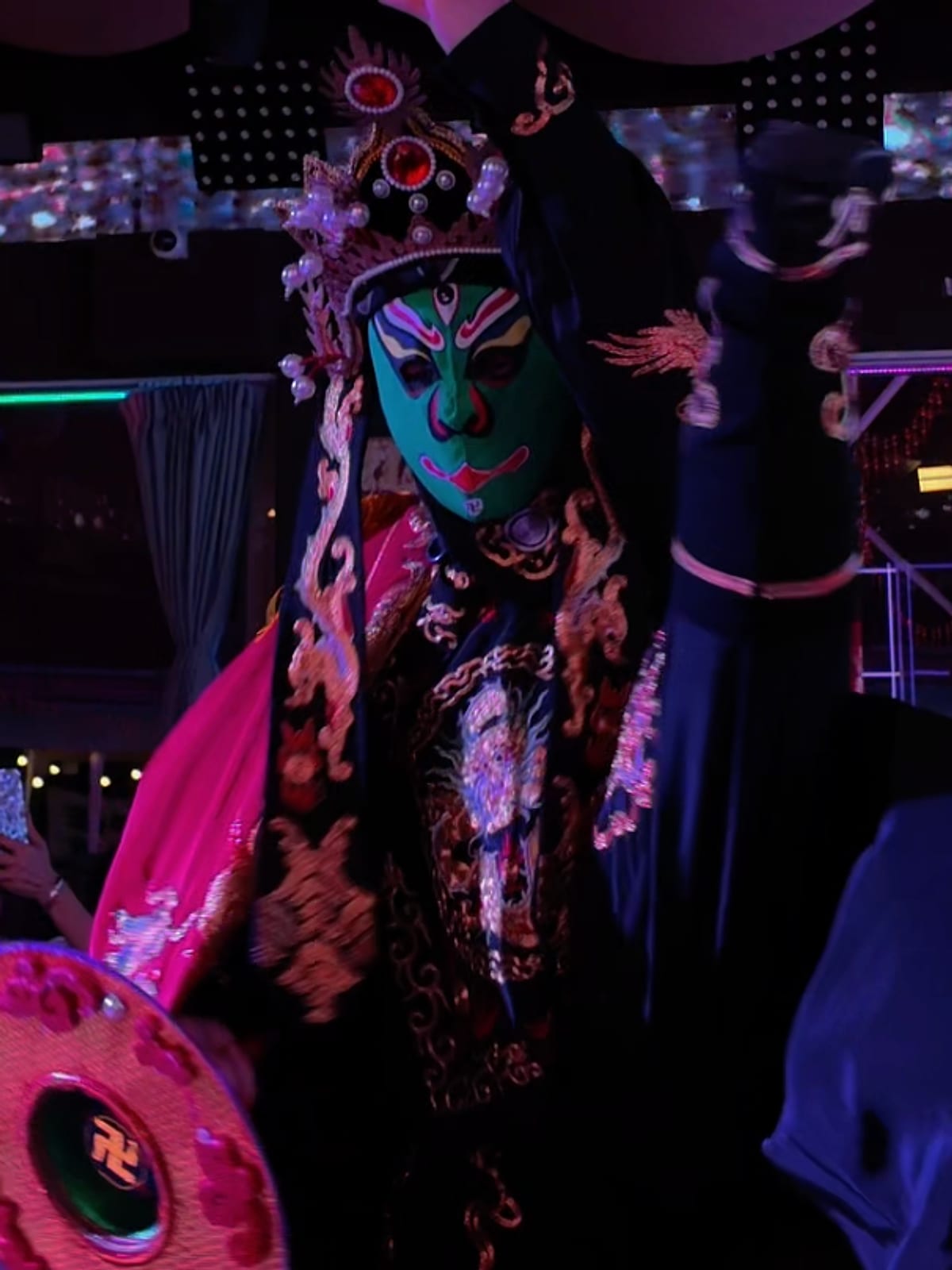 A Bian Lian performer in an ornate costume and painted face changing mask on stage