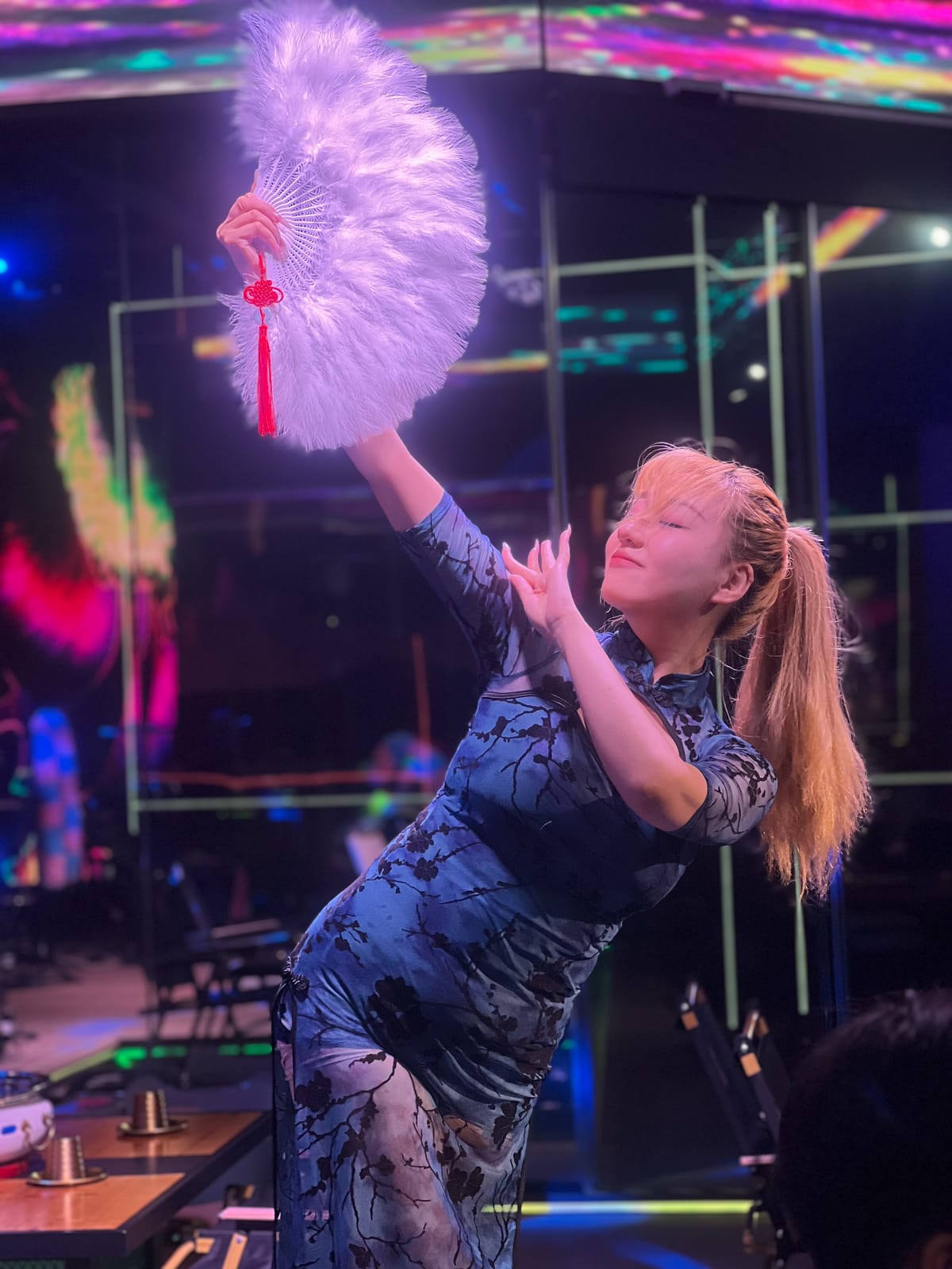 A dancer performing with a feather fan on stage at Xin Yan